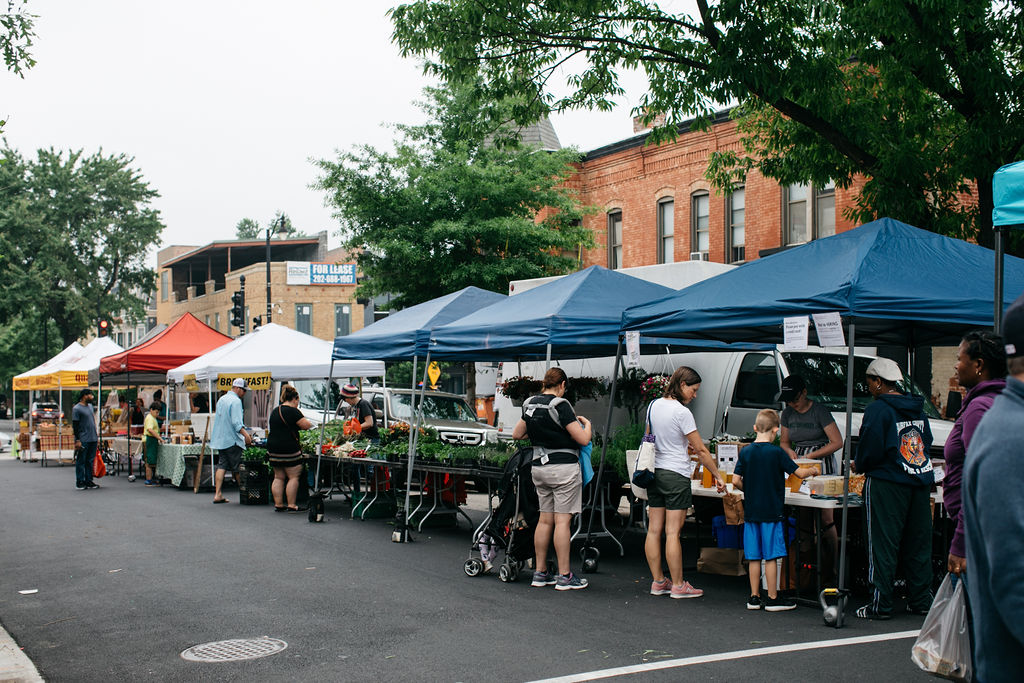 Tents stand on the street at the H Street NE market; families and adults shop for groceries, plant starts, pasture-raised meats, and more.